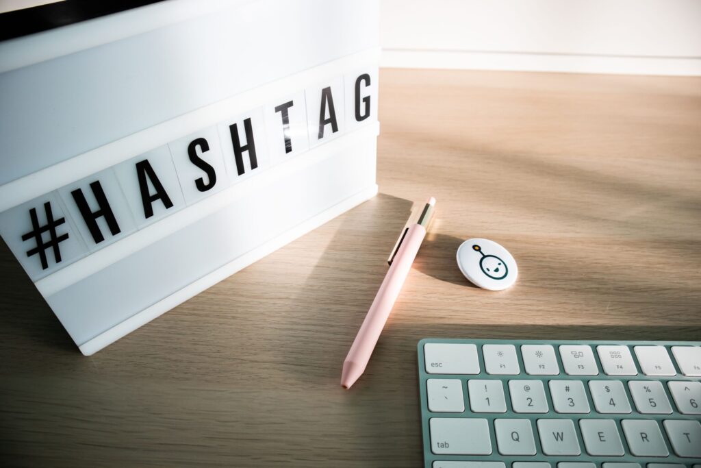 A minimalist desk setup featuring a hashtag lightbox, keyboard, and pen under natural sunlight.