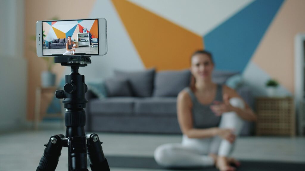Female fitness vlogger using smartphone to record a session in stylish living room.